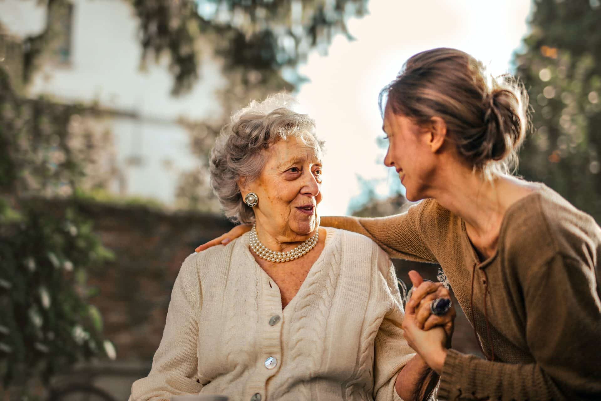 A young woman talking with an elderly woman while holding her hand.