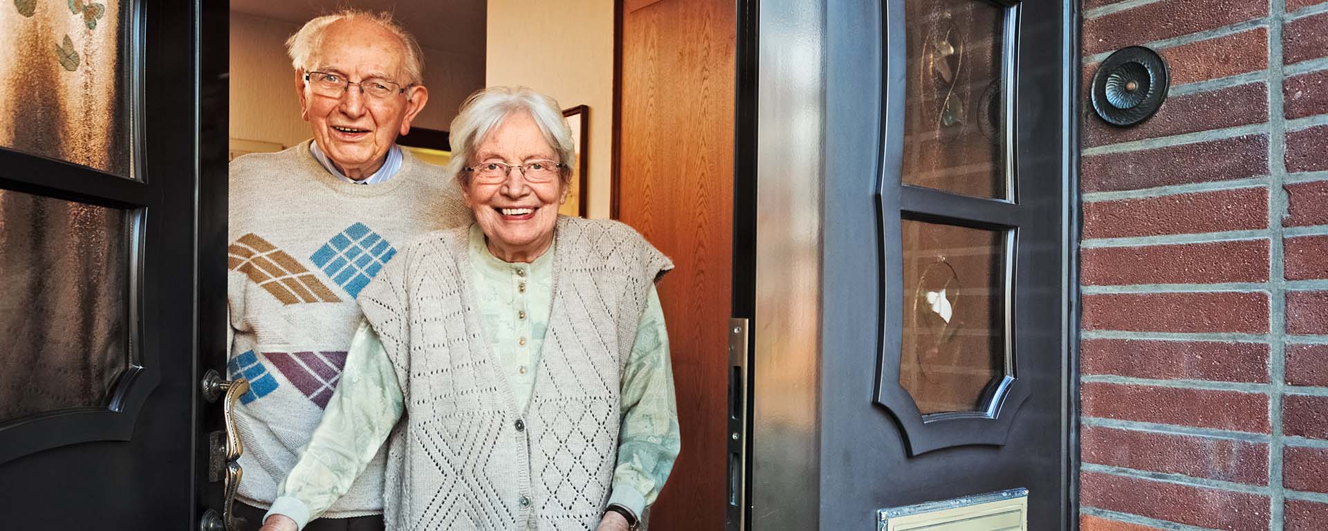 Elderly couple standing in the doorway of their home.