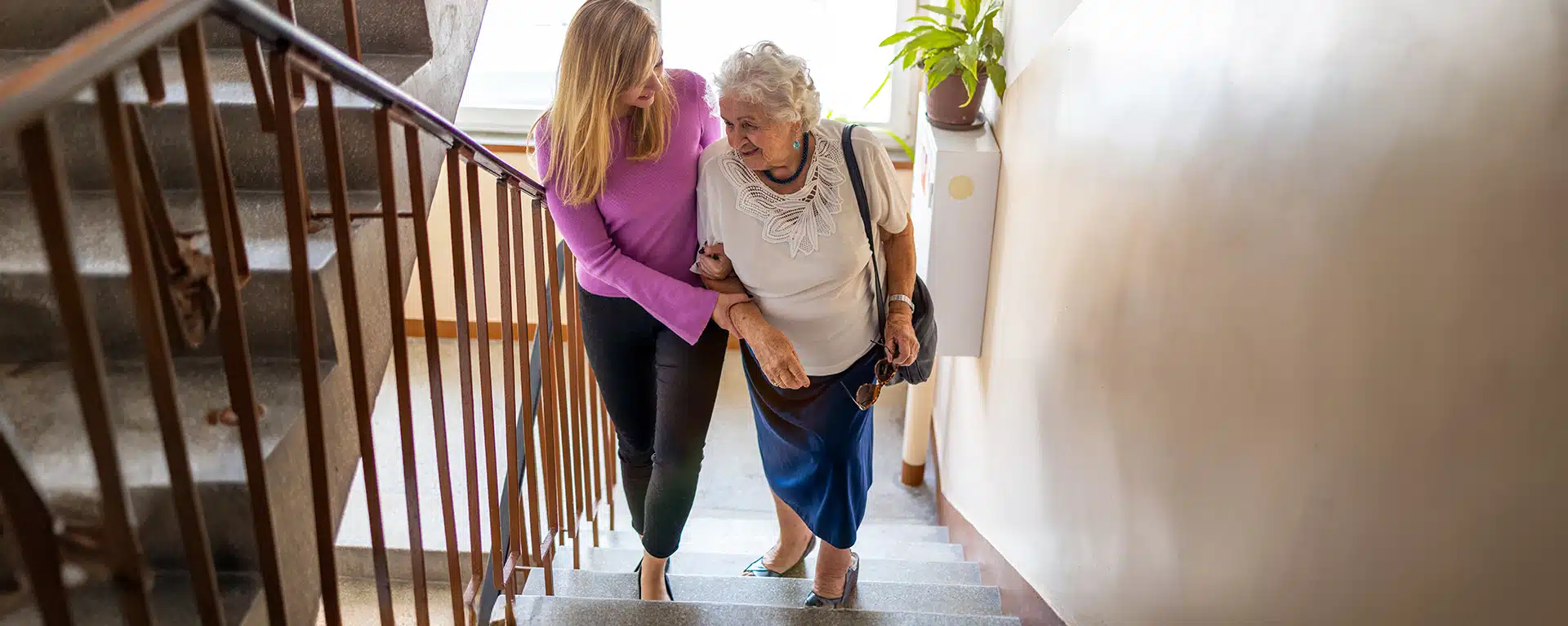 A young woman helps a senior woman up the stairs.