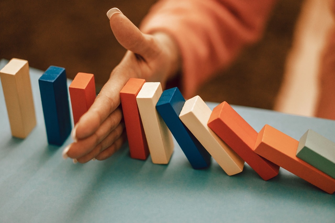 Dominos falling into each other, with a womans hand stopping the collapse