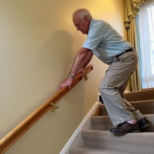 Older man struggling to walk down the stairs using both hands on the railing